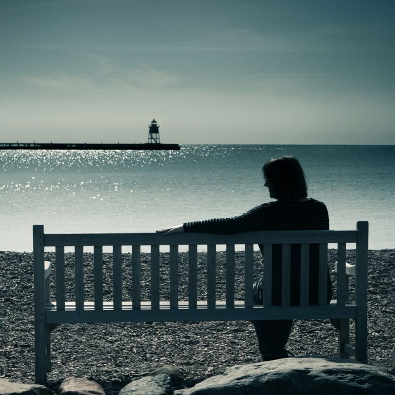 older woman on a bench at the beach in Roseville, CA, after her spouse passed away